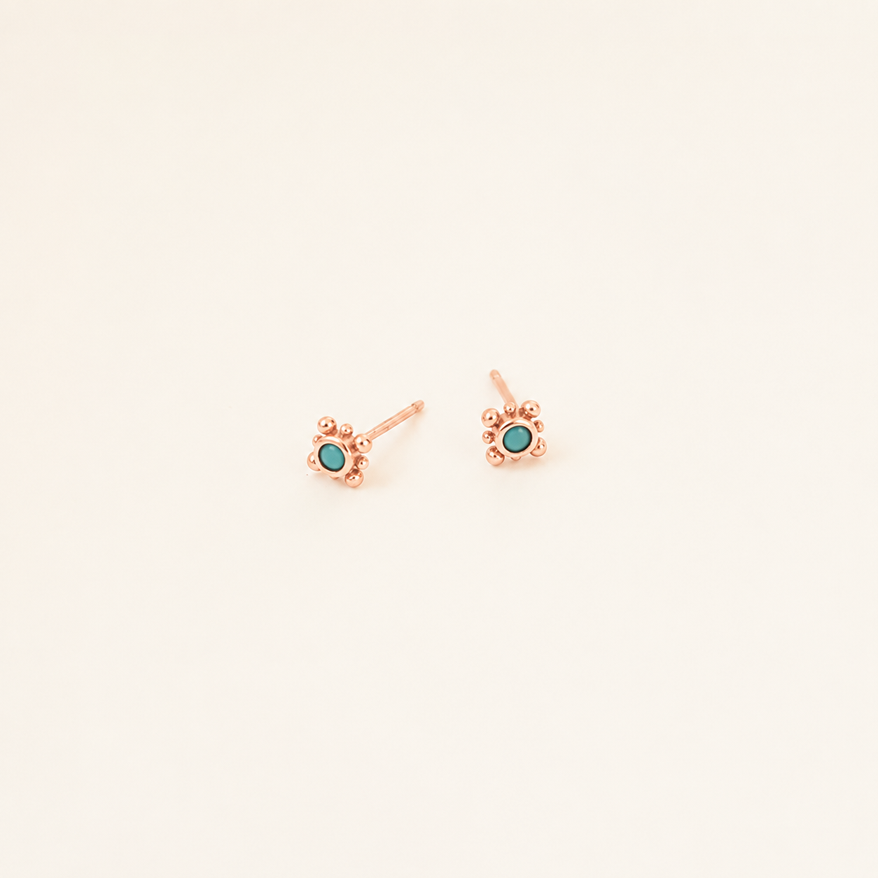 Rose gold earrings with turquoise stones on a light beige background
